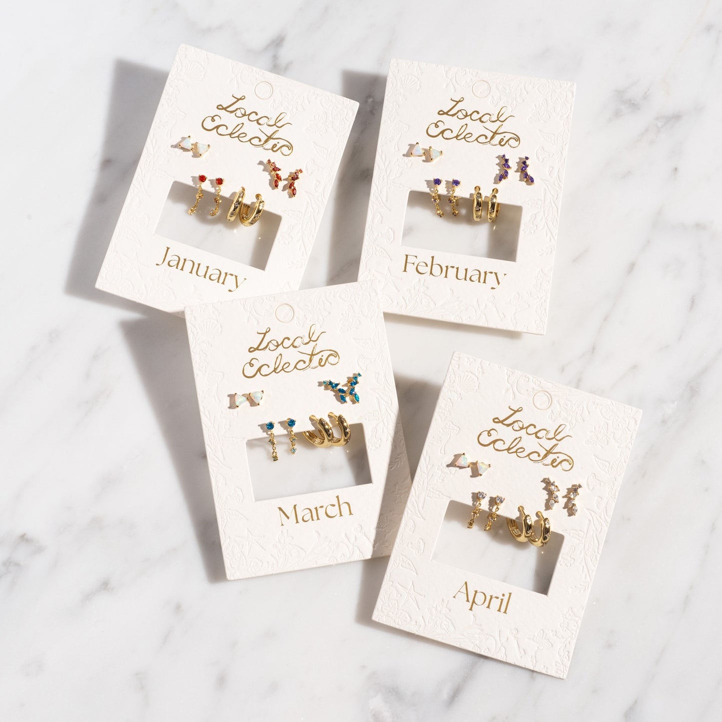 Four Classic Birthstone Earring Sets for January, February, March, and April are shown on white cards with gold “Local Eclectic” text. Each 14k gold plated set features unique colored stones and designs for a personalized ear stack.