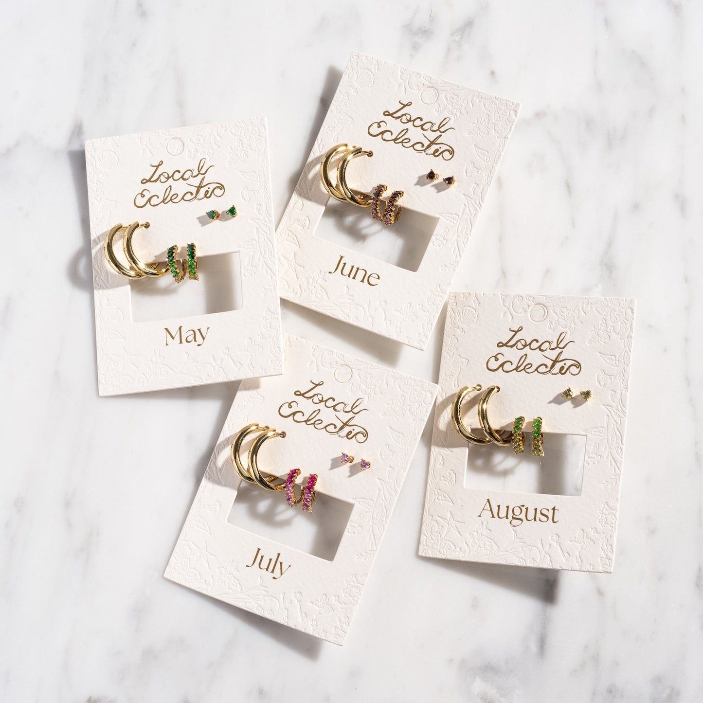 The Bold Birthstone Earring Set features four pairs of gold plated hoop earrings with colorful gemstones for May, June, July, and August—perfectly displayed on embossed Local Eclectic cards for a personalized touch.