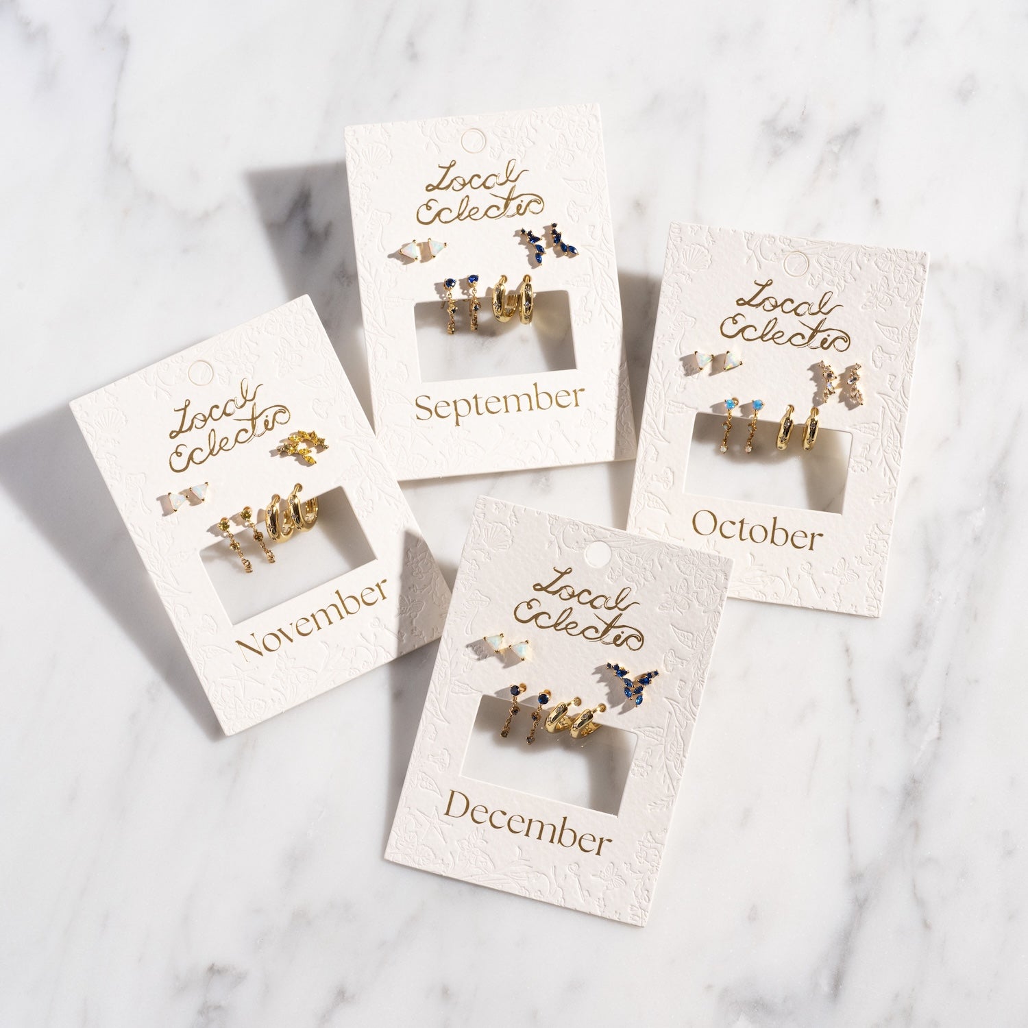Four Classic Birthstone Earring Sets, plated in 14k gold and labeled for September through December, perfect for a personalized ear stack, displayed on embossed Local Eclectic cards atop a white marble surface.