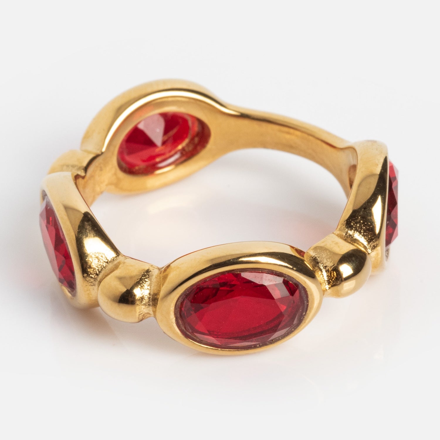 The Bita Ring is a gold band adorned with four evenly spaced, oval-shaped faceted red gemstones, captured against a white background.