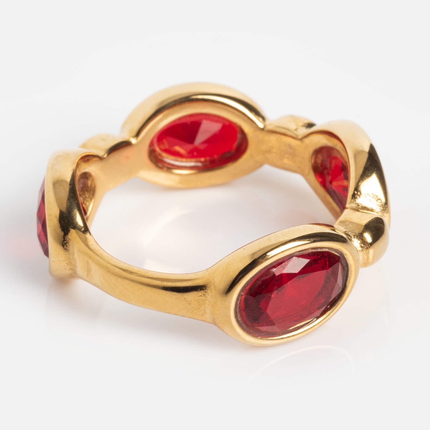 The Bita Ring is a gold band adorned with evenly spaced oval red gemstones in bezel settings, finished with a polished shine.