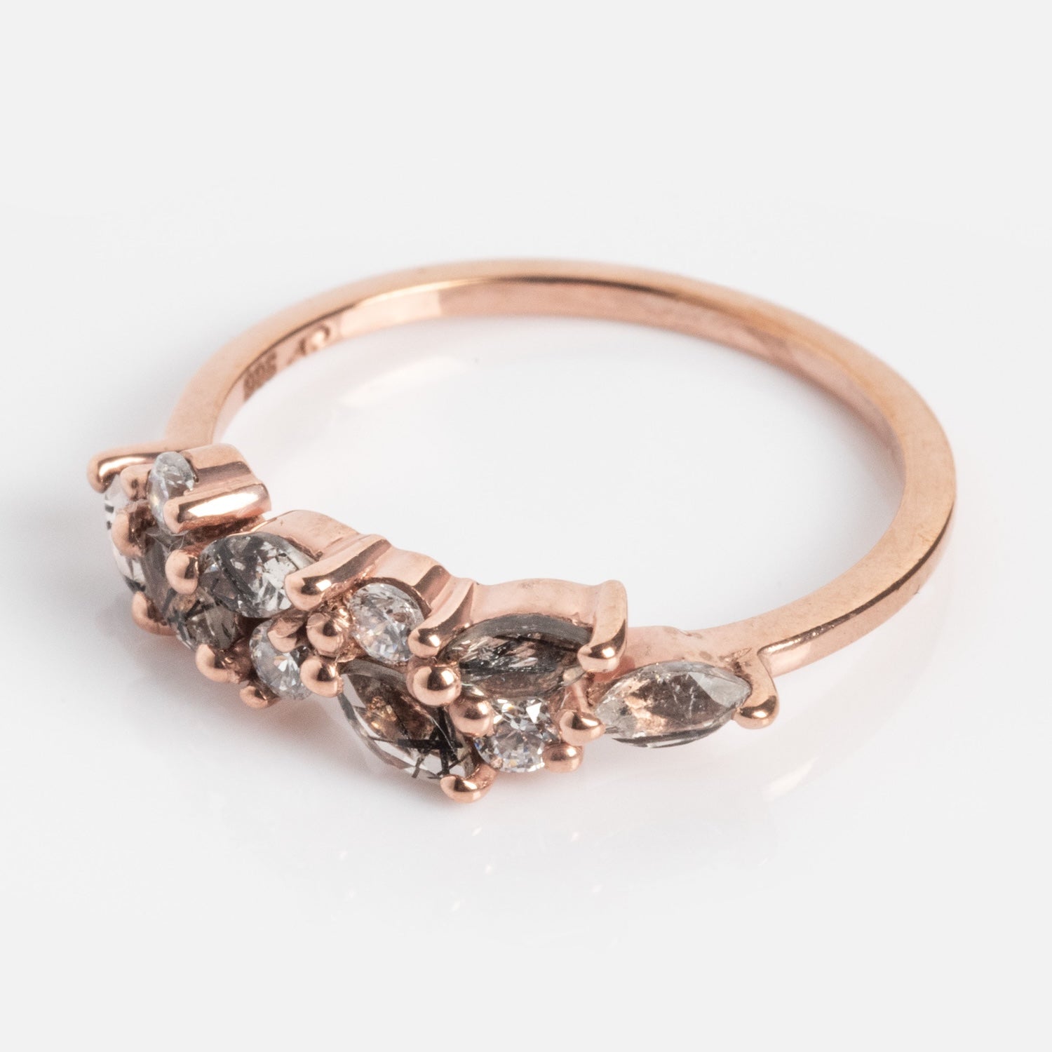 The Gemstone Orchard Ring showcases London blue topaz and clear gemstones in prong settings along the top half of its rose gold band, displayed on a white background.