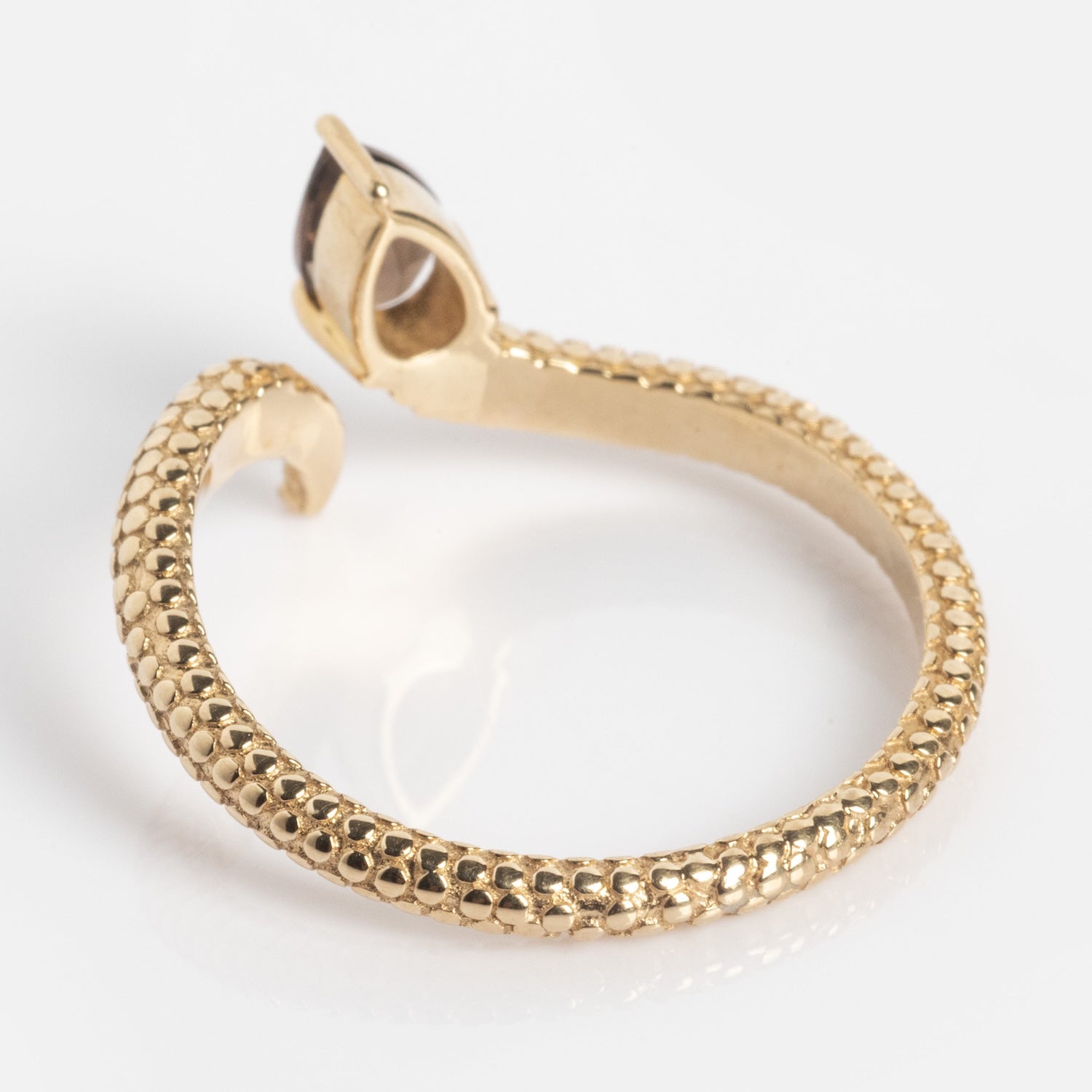 The Solid Gold Smoky Quartz Snake Ring for Transformation features a gold textured, snake-like open band with a bezel-set smoky quartz gemstone. This Local Eclectic exclusive is showcased elegantly on a white surface.