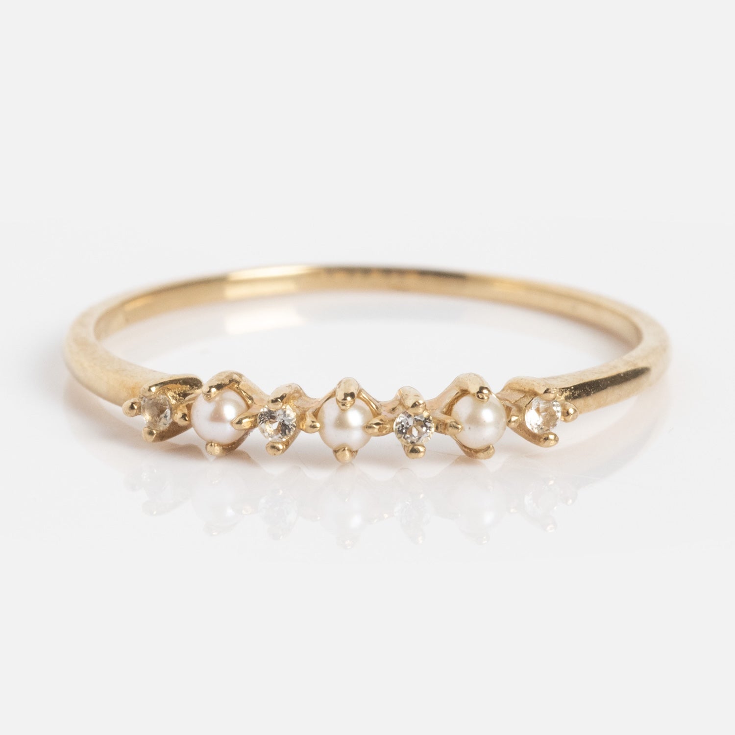 The Solid Gold Pearl Trio Ring features a thin yellow gold band with an alternating pattern of small freshwater pearls and sparkling diamonds, showcased on a plain white background.
