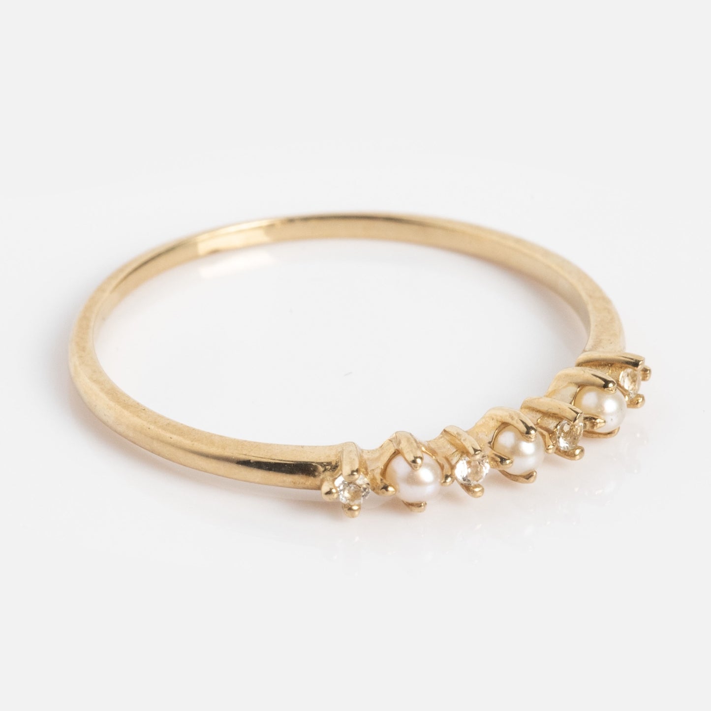 The Solid Gold Pearl Trio Ring is a slim yellow gold band with sparkling stones and freshwater pearls in an alternating row, shown on a white background.