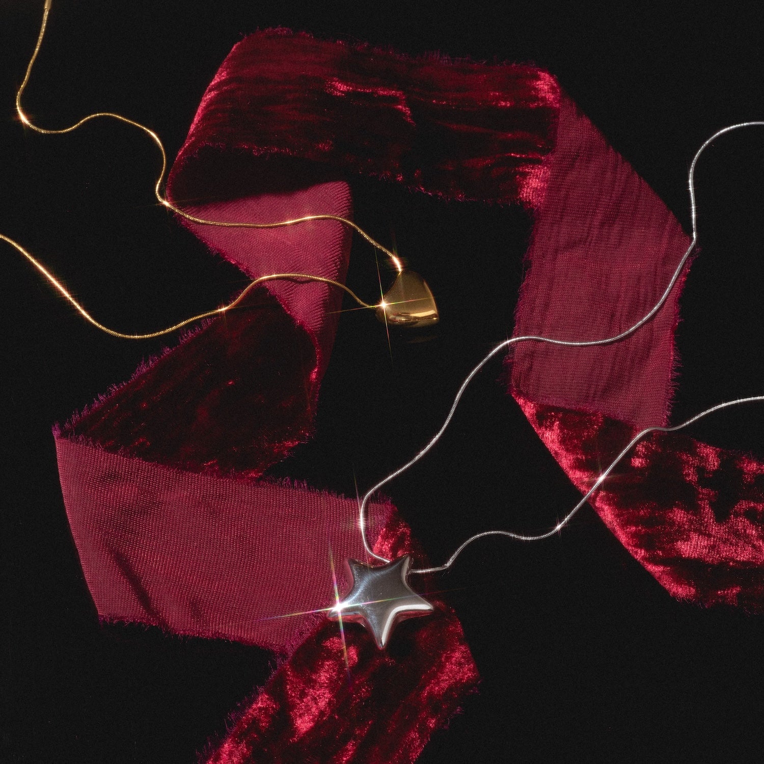 The Yellow Necklace features gold heart and silver star pendants on a deep red velvet ribbon, set against a black background with glowing string lights.