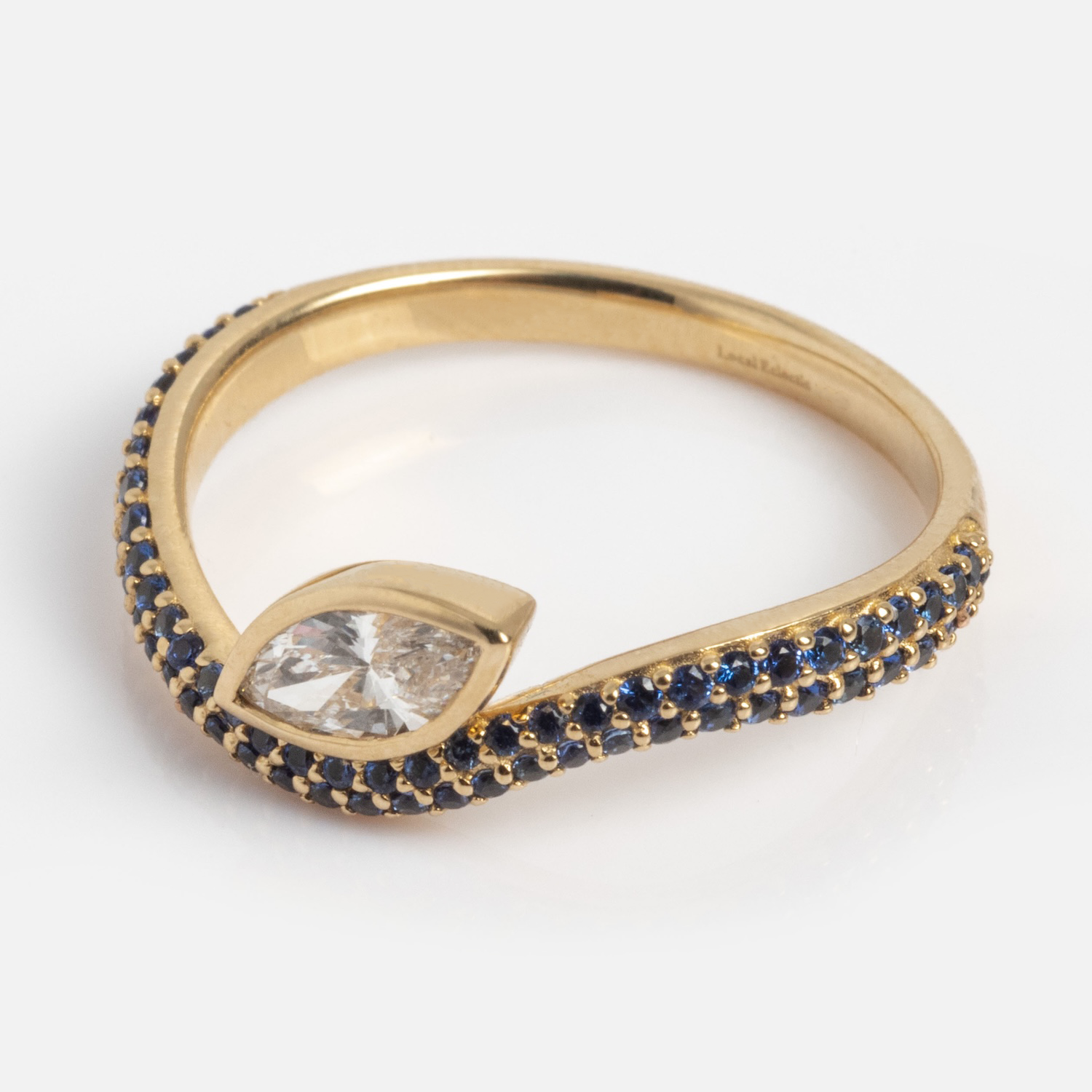 The Solid Gold Nesting Gleam Sapphire and Diamond Ring features a marquise-cut diamond and a gold band adorned with small blue sapphires in two rows along the twisting design, shown on a white background.