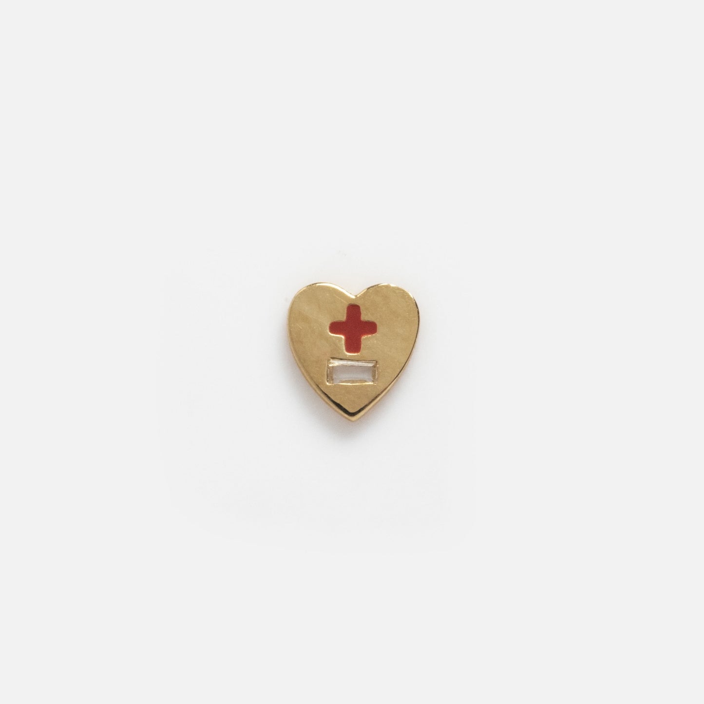 The Solid Gold Tiny Lucky Charm for Glass Charm Locket is a gold heart-shaped pin inspired by yellow gold charms, featuring a red cross above a blank white rectangle on a plain white background.