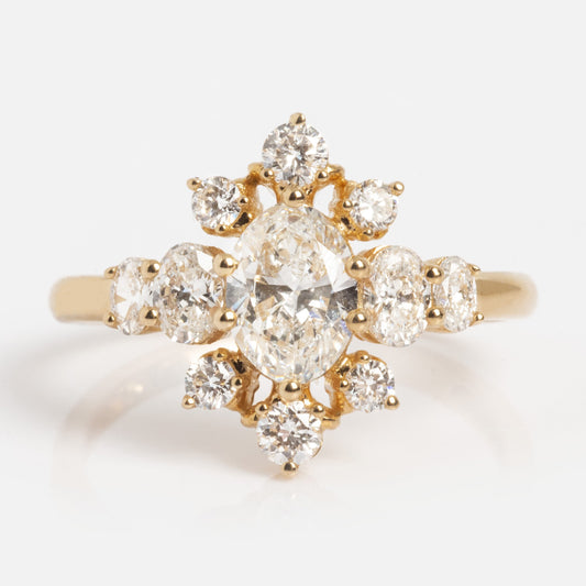 The 14k Floating Deco Cluster Diamond Ring features a central oval diamond accented by smaller round diamonds in a starburst cluster, all set in gold against a plain white background.