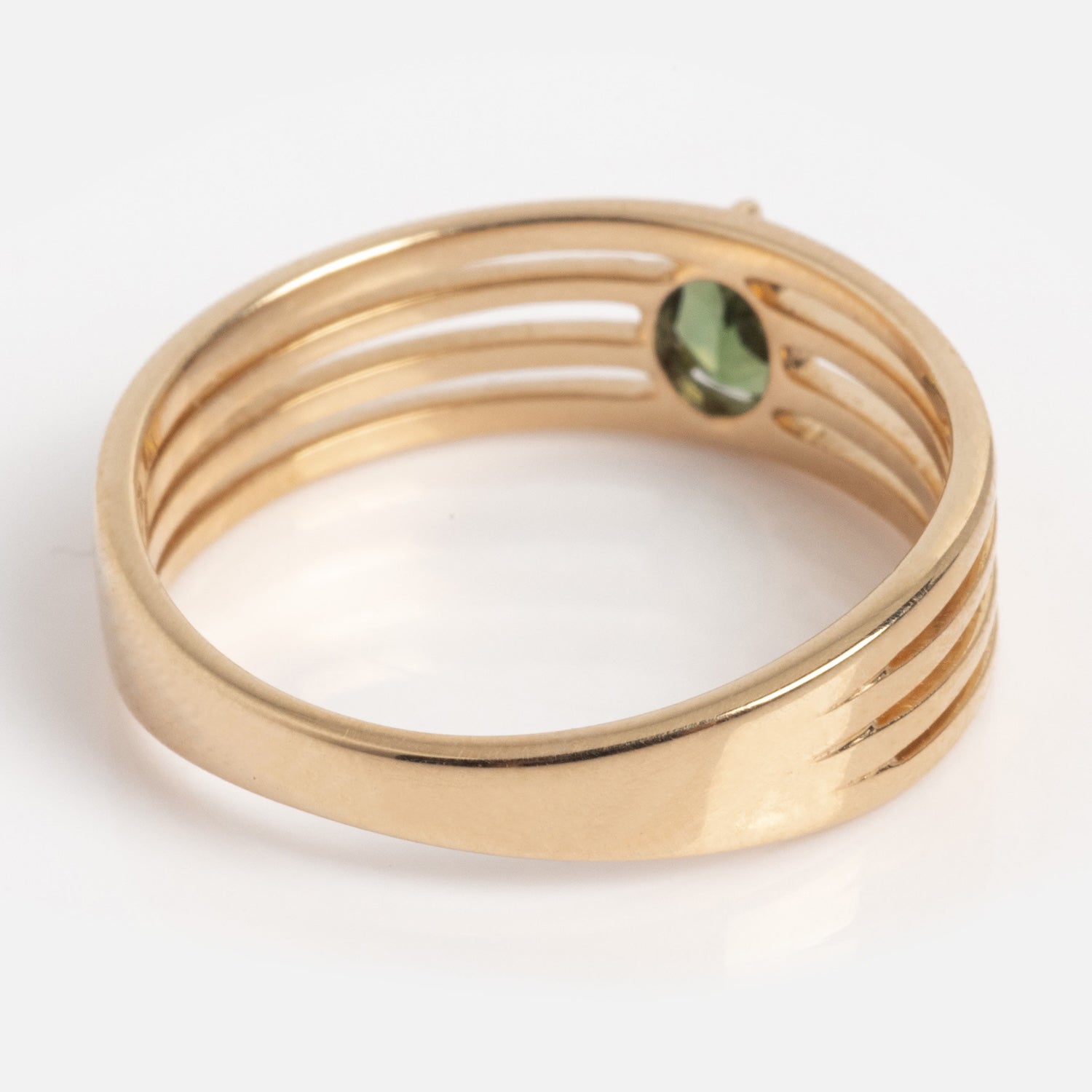 The Solid Gold Stacked Horizon Tourmaline Ring features four parallel grooves, an open design, and a small round green tourmaline set on one side. It is displayed on a white background.