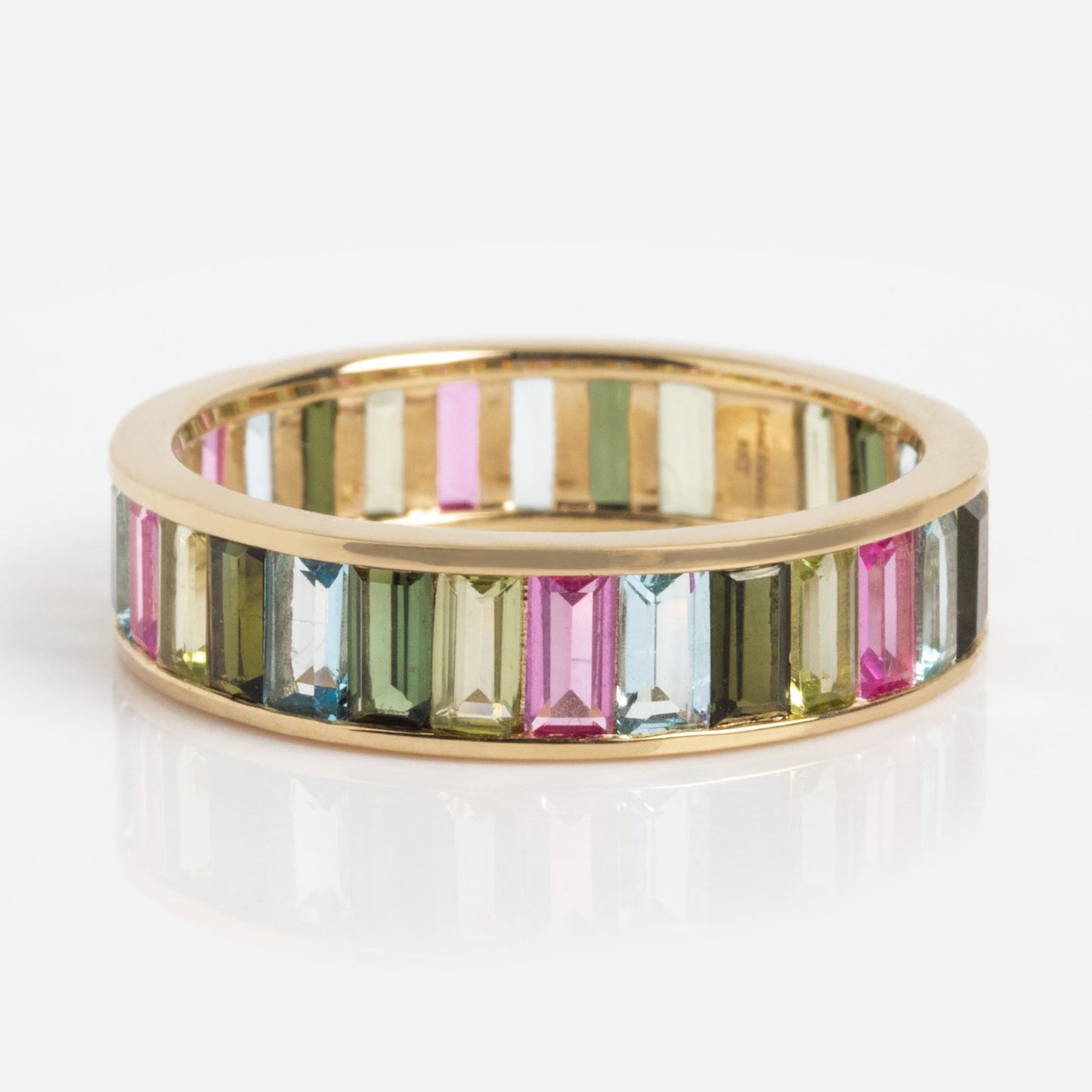 The Solid Gold Gemstone Kaleidoscope Eternity Band showcases a continuous row of vertically set rectangular gemstones in pink, green, and blue hues encircling the entire gold band.