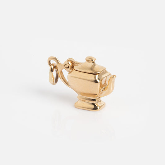 A Vintage 14k Tea Pot Charm shaped like a small gold teapot with a handle, spout, and lid is displayed on a white surface.