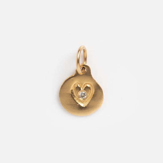 The Vintage 14k Art and Craft Diamond Heart Charm is a small round gold pendant with a central heart-shaped engraving featuring a clear diamond. It includes a top loop for attaching to a chain.