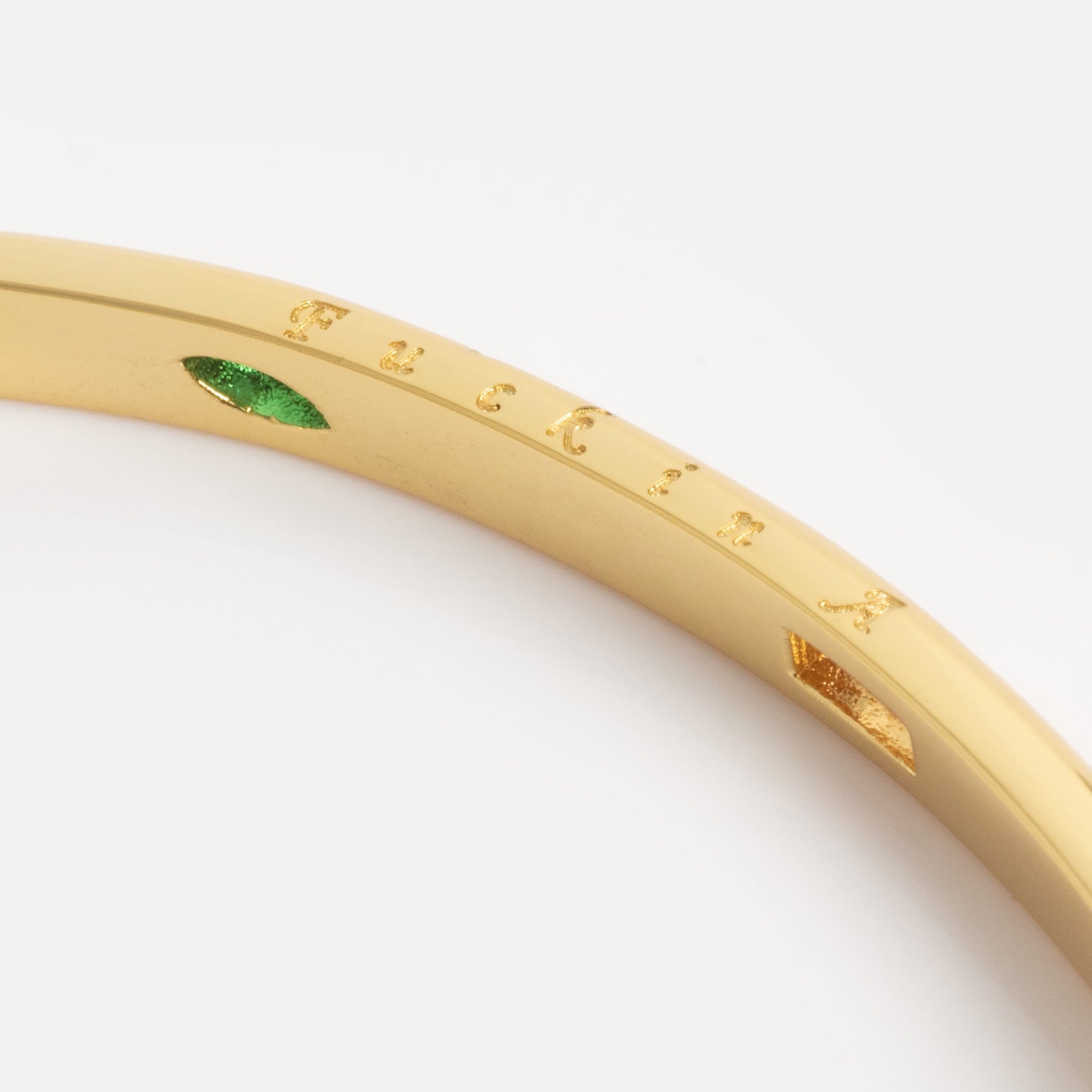 A close-up of the Hidden Curse Word Fuck Off Bracelet—gold with engraved letters and a green marquise-shaped gemstone—on a plain white background.