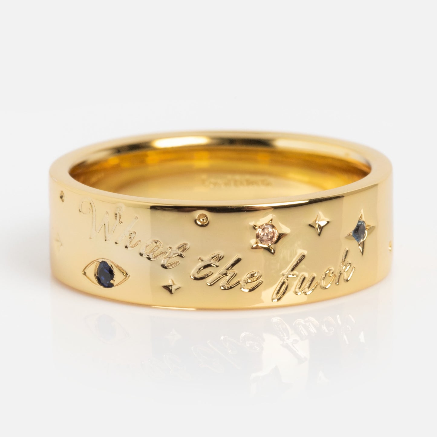 The What the Fuck Cigar Band is a gold ring engraved with "What the fuck" and features star, eye, and gemstone designs on a plain white background.