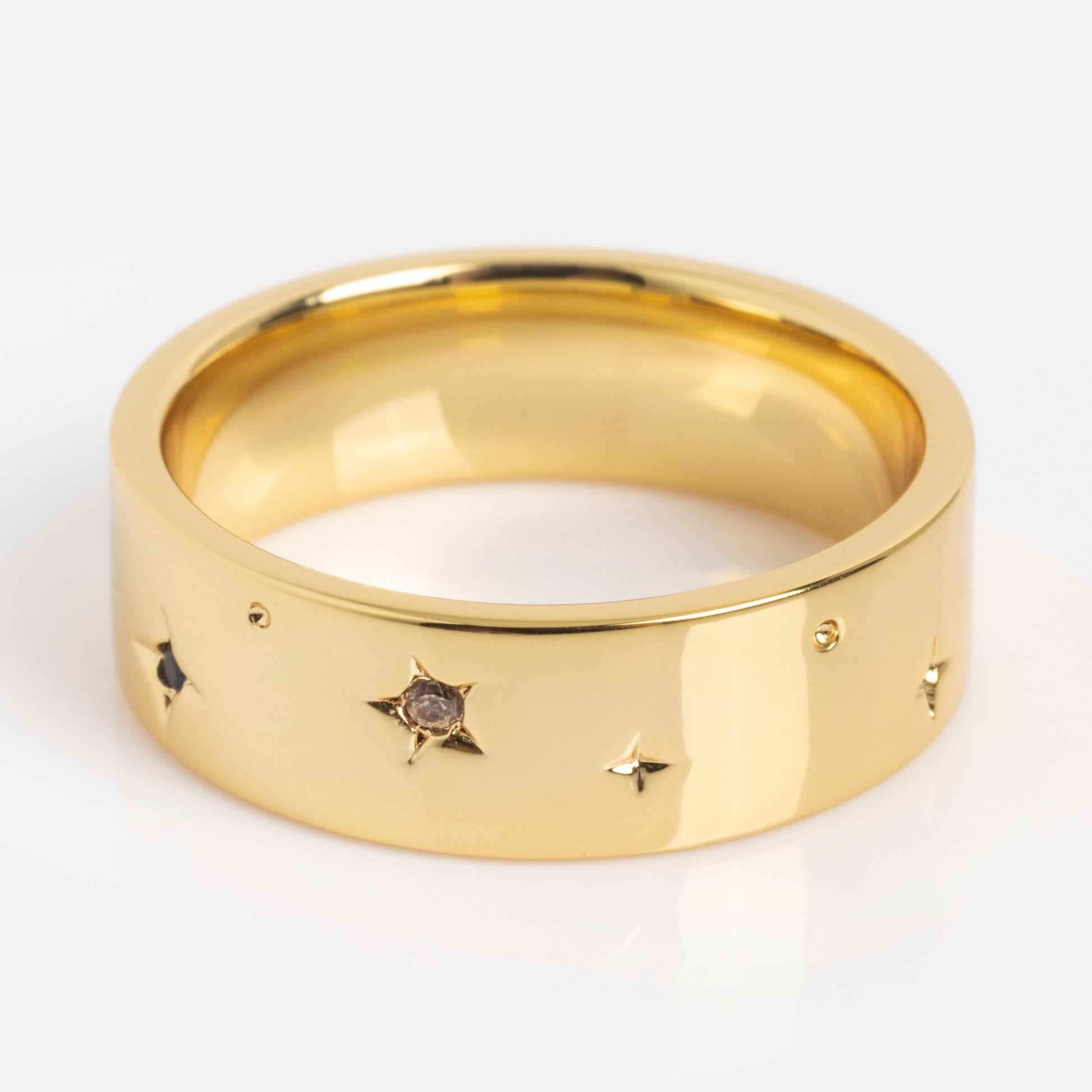 The What the Fuck Cigar Band is a wide gold ring with a smooth, polished finish, adorned with small star-shaped engravings—some set with tiny gemstones.