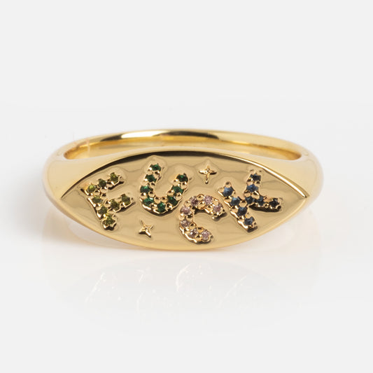 The Colorful Language Fuck Signet Ring is a gold ring with an oval face, featuring the word "FUCK" in colorful gemstones. Set against a plain white background.