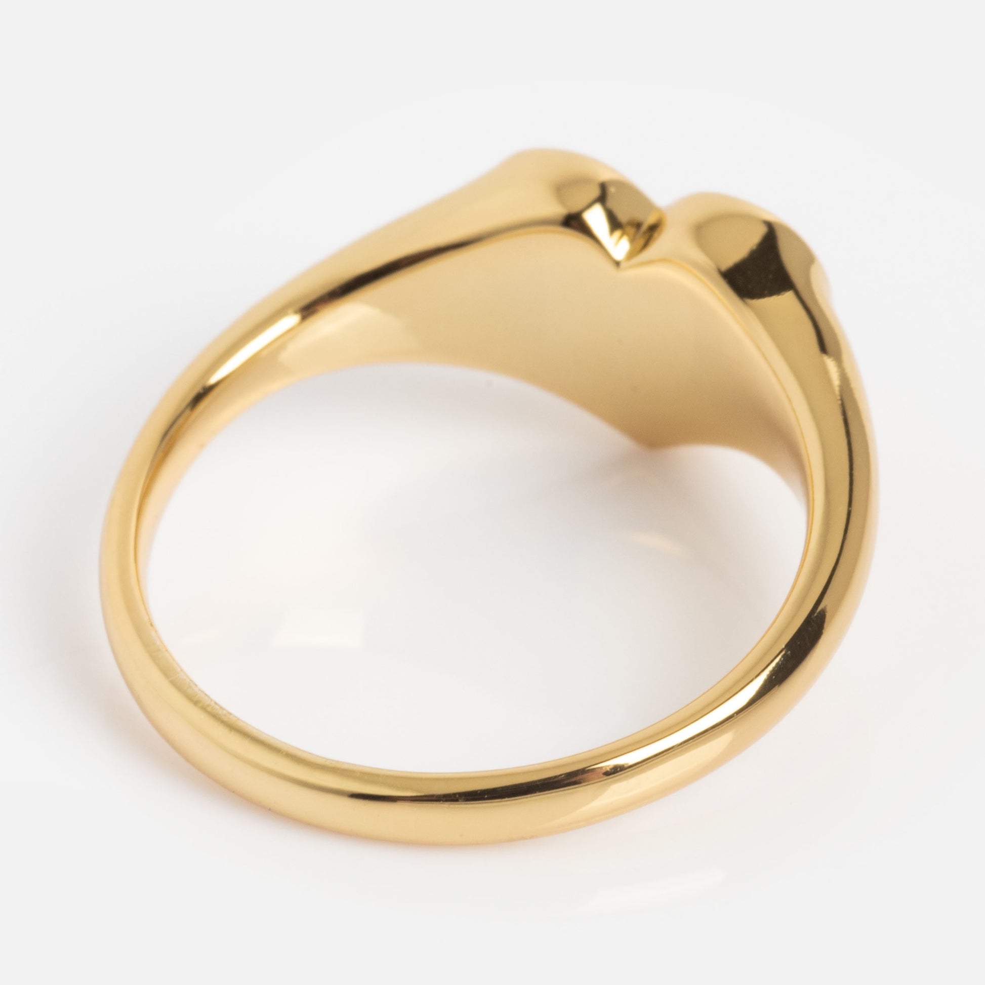 The Tiny Cunt Signet Ring features a unique sculpted design on top, shown at an angle to accentuate its shiny gold surface and elegant curves, all set against a plain white background.