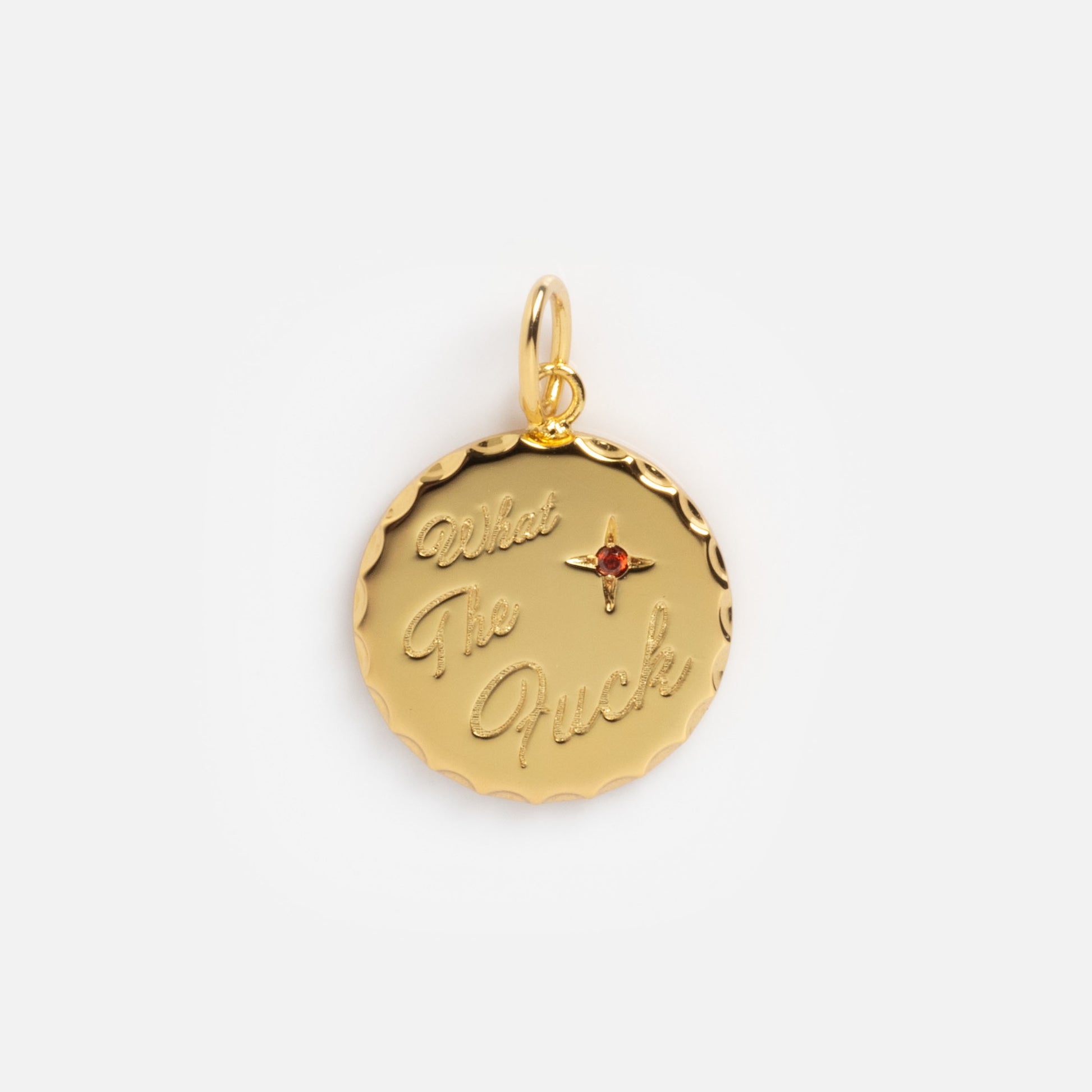 The Curse Word Charm is a round gold pendant with engraved cursive text reading "What The Fuck," a small red gem in a star shape above "Fuck," scalloped edges, and a loop for attaching to your chain.