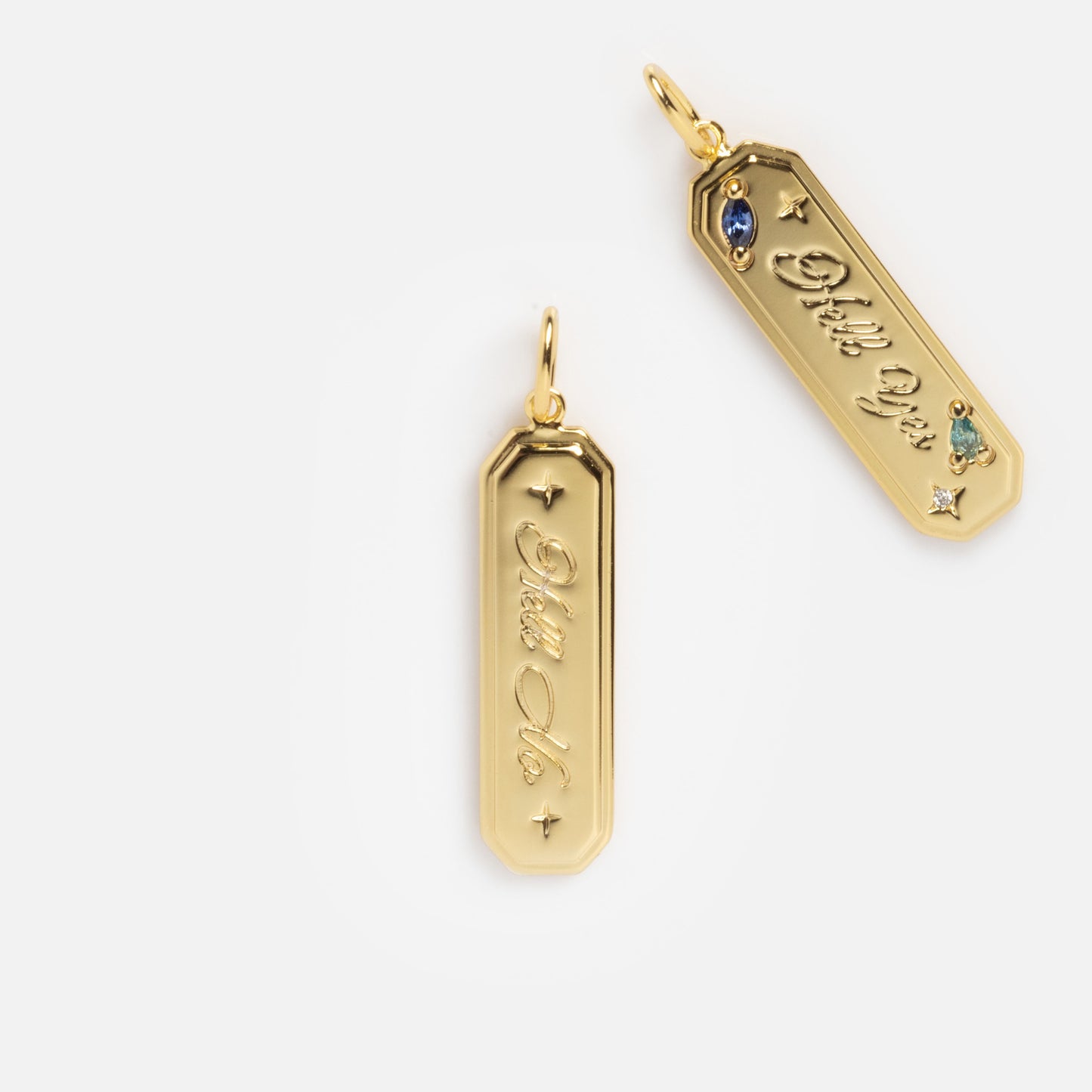 The Curse Word Charm features two shiny gold rectangular pendants with beveled edges; one is engraved "Ditto You" with three gemstones, and the other "Ditto Me" with one gemstone, both displayed on a white background.