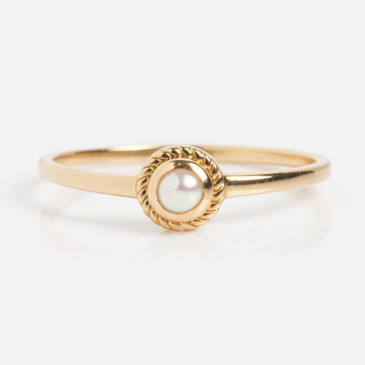 The Solid Gold Soft Glow Pearl Ring is a vintage-inspired piece with a round pearl at the center, accented by a twisted gold border and displayed on a white background.