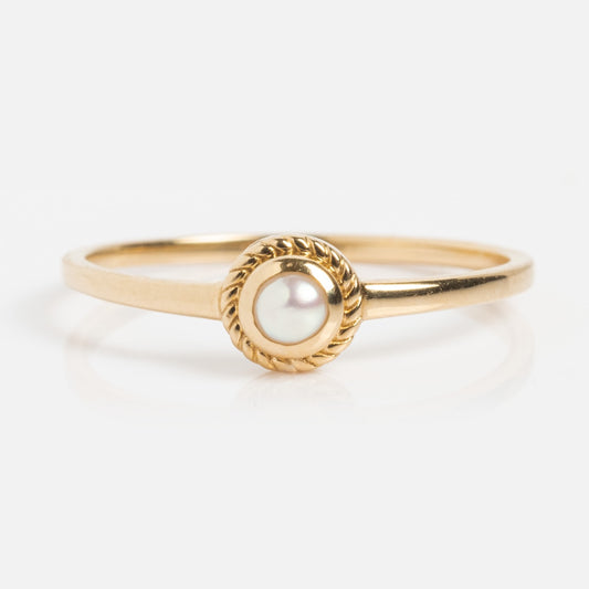 The Solid Gold Soft Glow Pearl Ring is a vintage-inspired piece with a round pearl at the center, accented by a twisted gold border and displayed on a white background.