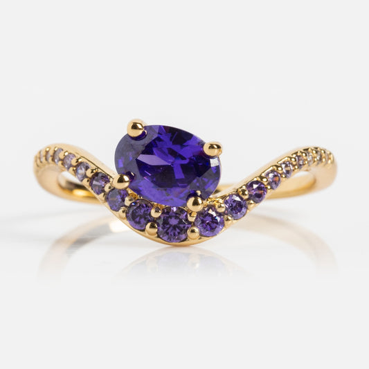 The Main Character Floating Ombre Birthstone Ring features a large oval-cut deep purple gemstone centerpiece, accented by smaller round purple stones on a gracefully curved gold band—an elegant birthstone jewelry addition.