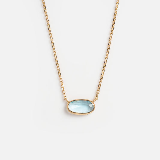 The Solid Gold Daybreak Swiss Blue Topaz Necklace features an oval-shaped Swiss blue topaz pendant in a simple gold bezel, shown on a plain white background. It belongs to the timeless Family Gold collection.