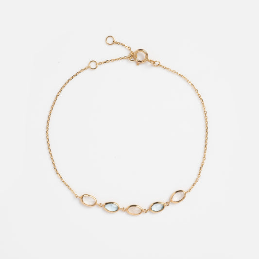 The Solid Gold Daybreak Moonstone and Blue Topaz Bracelet showcases five oval gemstones in a row with an adjustable length and spring ring clasp, beautifully displayed on a white background.