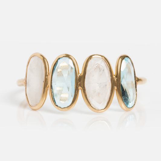 The Solid Gold Daybreak Moonstone and Blue Topaz Ring features four oval-cut stones—two blue topaz and two white moonstones—set vertically in bezels on a plain white background.
