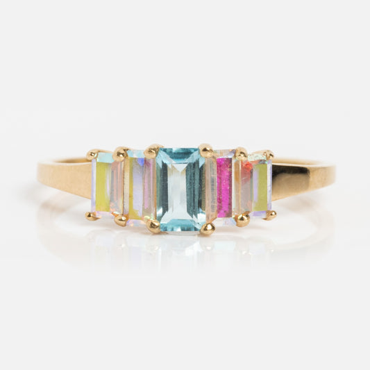 The Solid Gold Aurora Angel Aura Quartz and Blue Topaz Ring features five rectangular pastel gemstones—blue, pink, yellow, and green—set in prongs for a shimmering effect reminiscent of angel aura quartz.