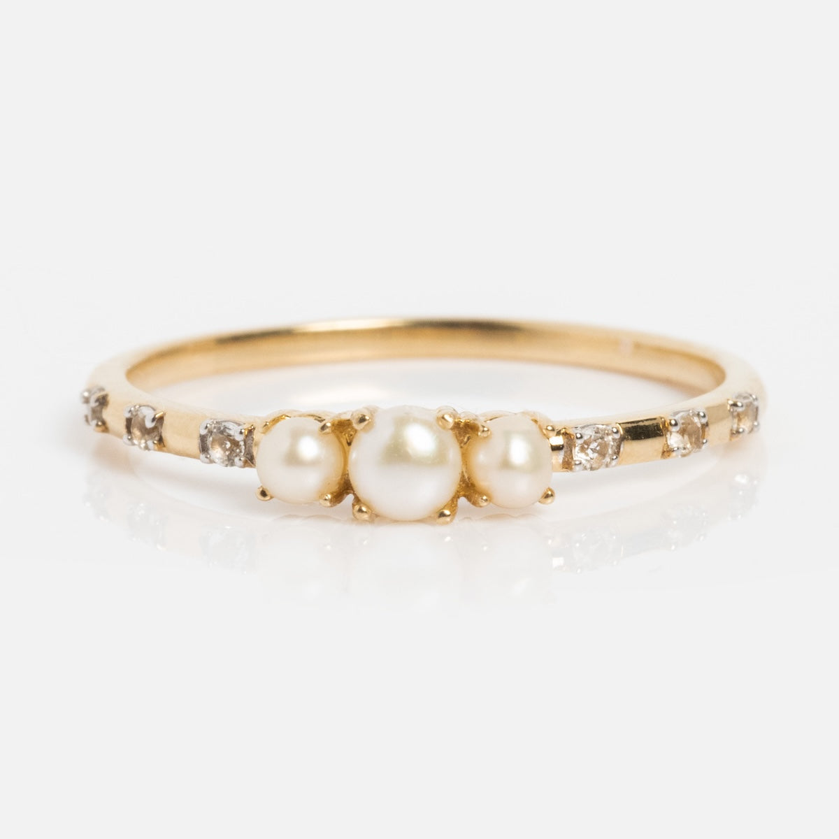 The Solid Gold Luminous Pearl Trio Ring features three central pearls and small diamonds on a solid gold band, elegantly displayed on a white background.