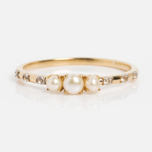 The Solid Gold Luminous Pearl Trio Ring features three central pearls and small diamonds on a solid gold band, elegantly displayed on a white background.