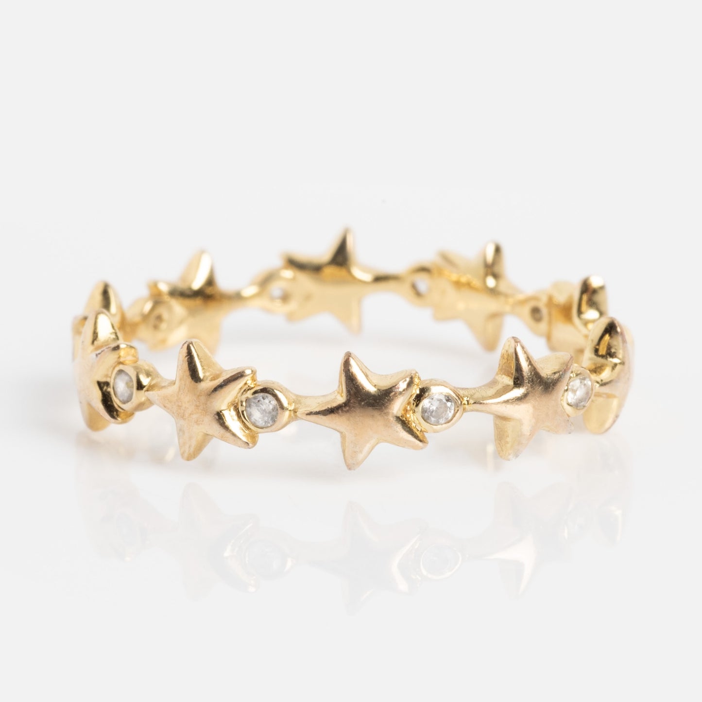 The Starlet Infinity Stacking Ring is a gold band with a continuous pattern of raised stars, each separated by a small round white gemstone, shown on a white background.