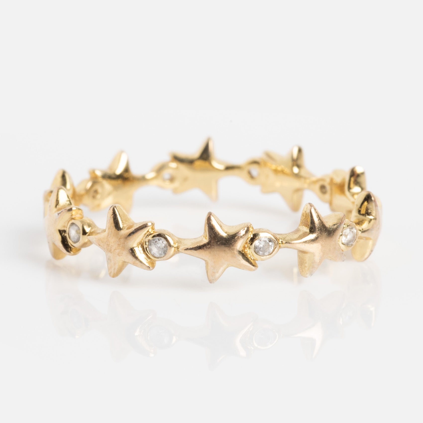 The Starlet Infinity Stacking Ring is a gold band with a continuous pattern of raised stars, each separated by a small round white gemstone, shown on a white background.
