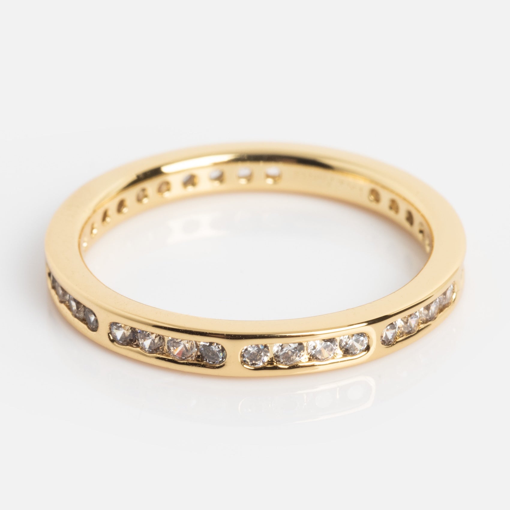 The Bold Eternity Stacking Ring features a row of small, clear gemstones set around a gold band, shown on a white background.