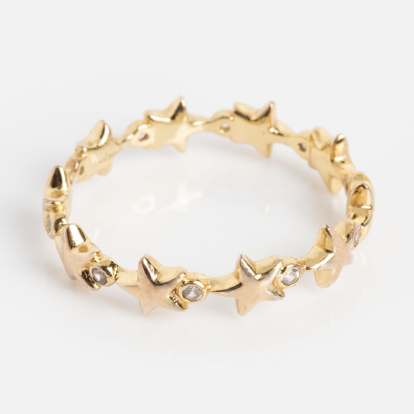 The Starlet Infinity Stacking Ring is a gold band with an endless pattern of small star shapes, some set with sparkling clear gemstones, shown against a plain white background.