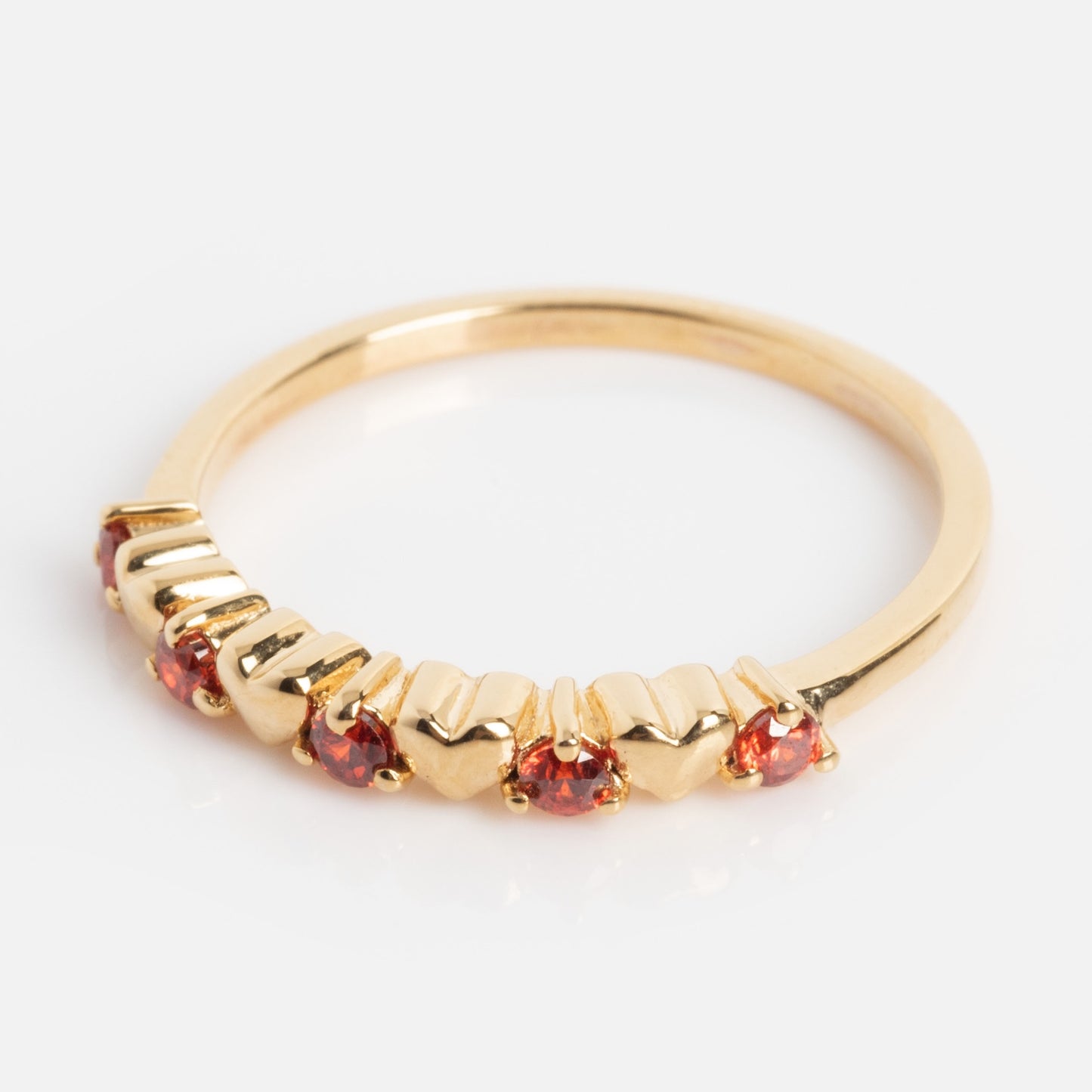The Sweetheart Stacking Ring is a gold band adorned with alternating small red gemstones and heart shapes, shown on a plain white background.