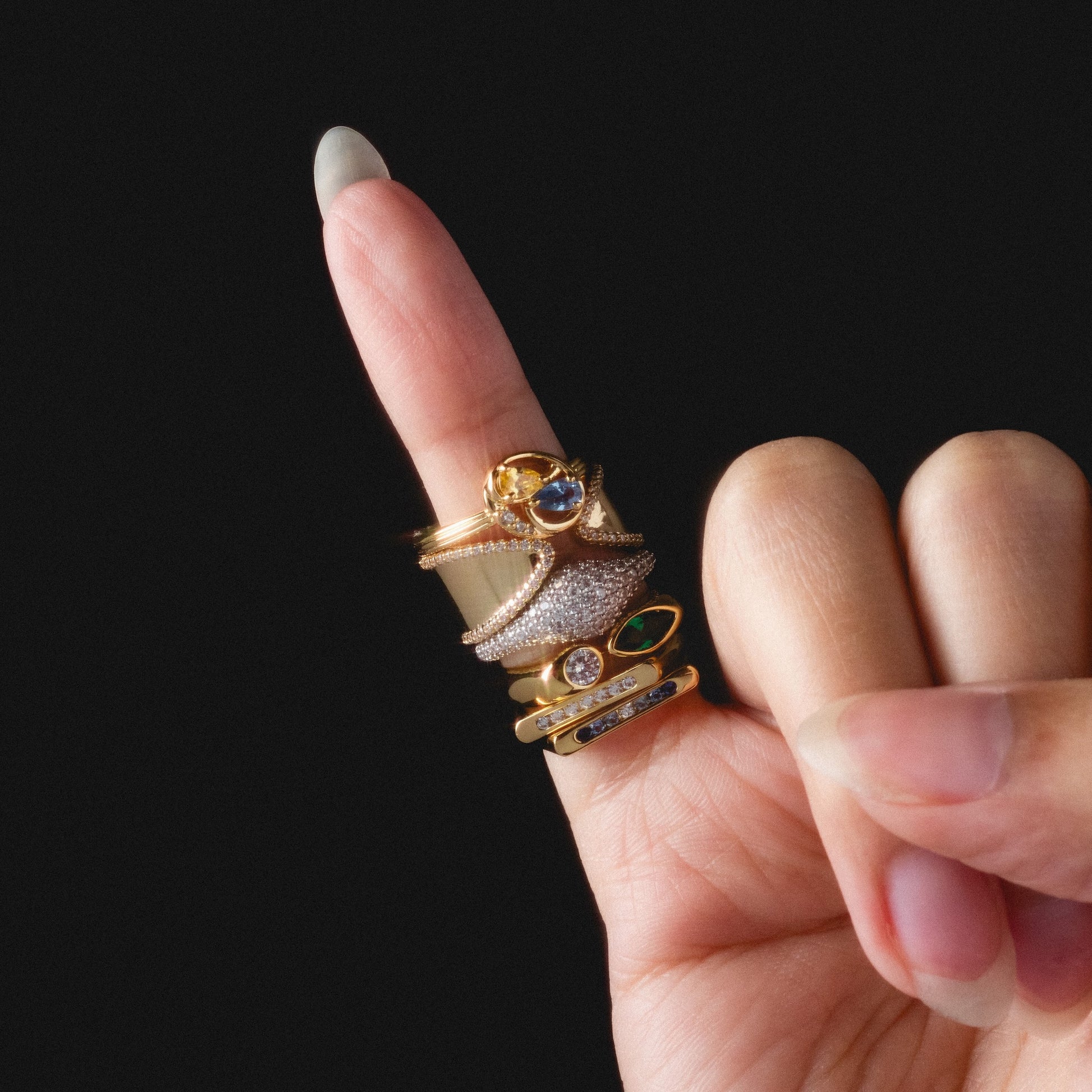 A manicured hand with a long nail displays the Open Front Cigar Pinky Ring, shining gold against a black background.