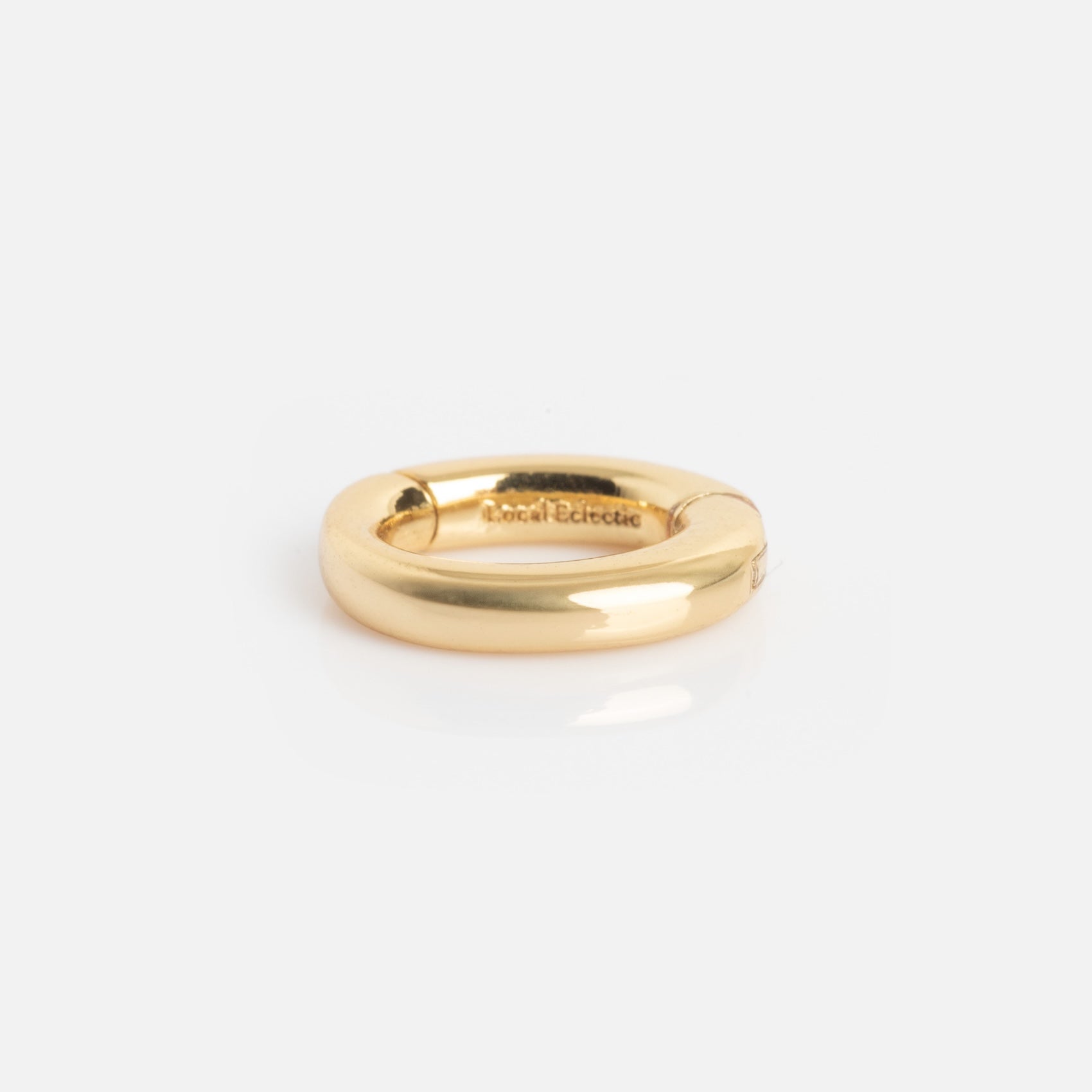 The Ring Clip is a shiny, thick gold ring with smooth, rounded edges, resting on a white background. Small text is engraved on its inner band.