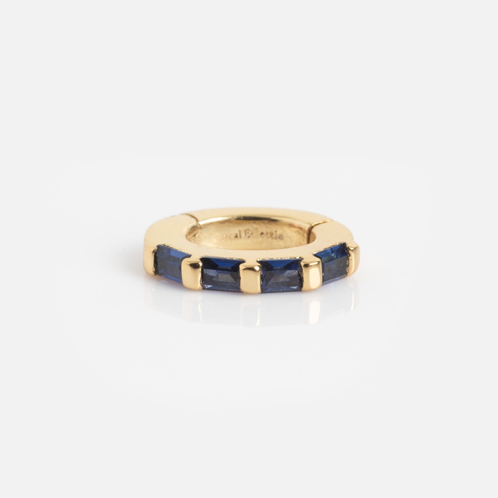 The Ring Clip is a small, circular gold ring featuring rectangular blue gemstones set along part of its edge, shown against a white background.