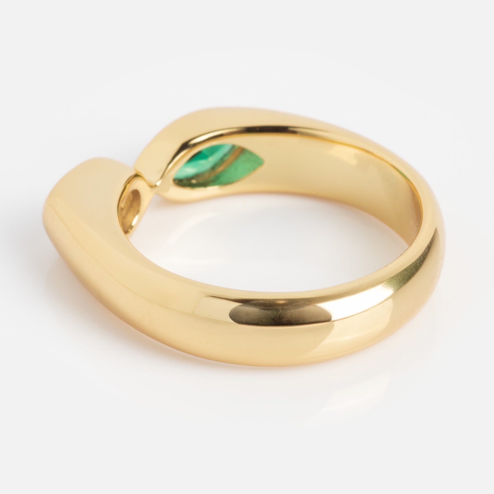 The Bold Toi Et Moi Pinky Ring features a modern, thick gold band that curves open at the top to reveal a small green gemstone set inside. Displayed on a white background.