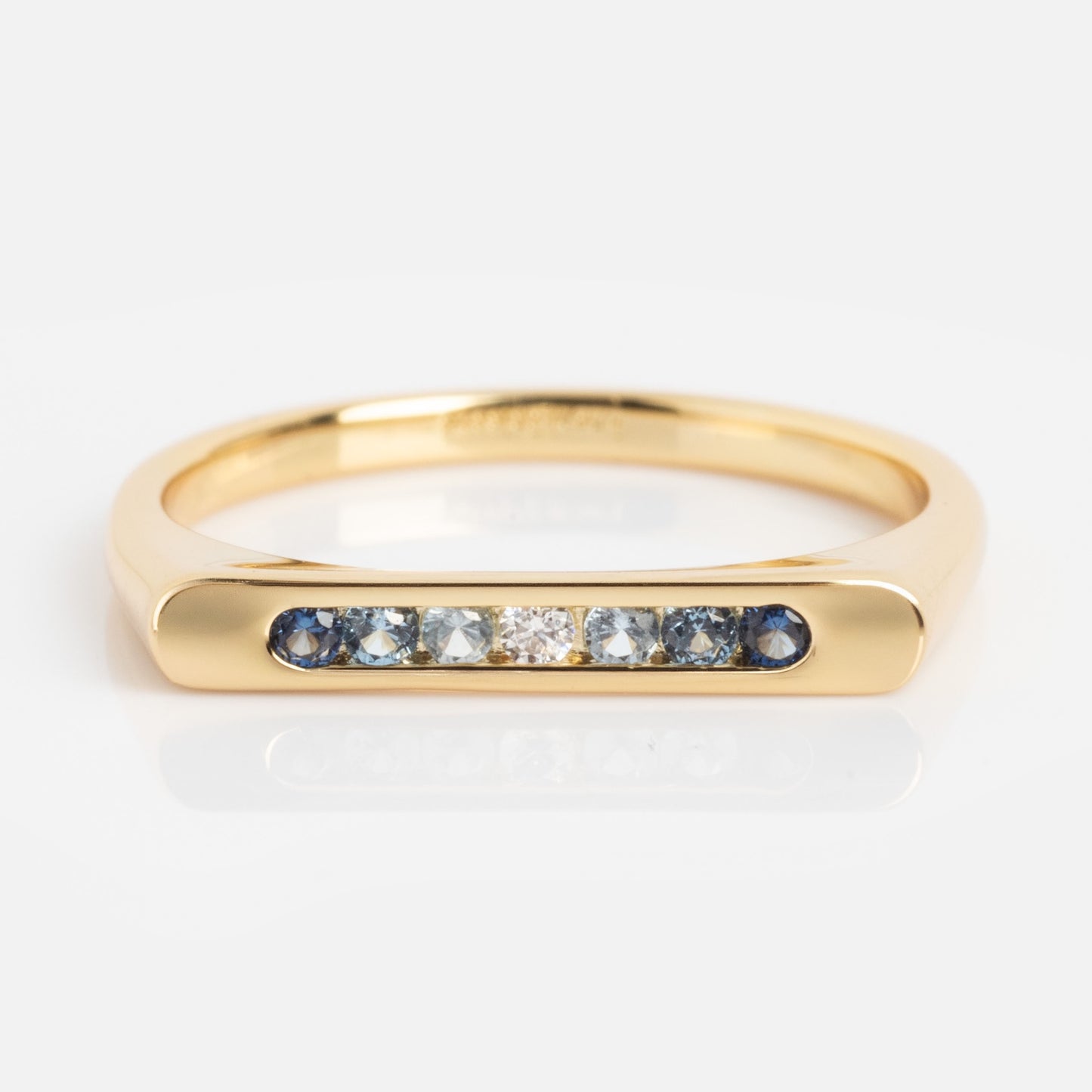 The Pave Bar Pinky Ring is a gold ring featuring a flat top adorned with five small blue gemstones and two clear center stones, shown against a white background.