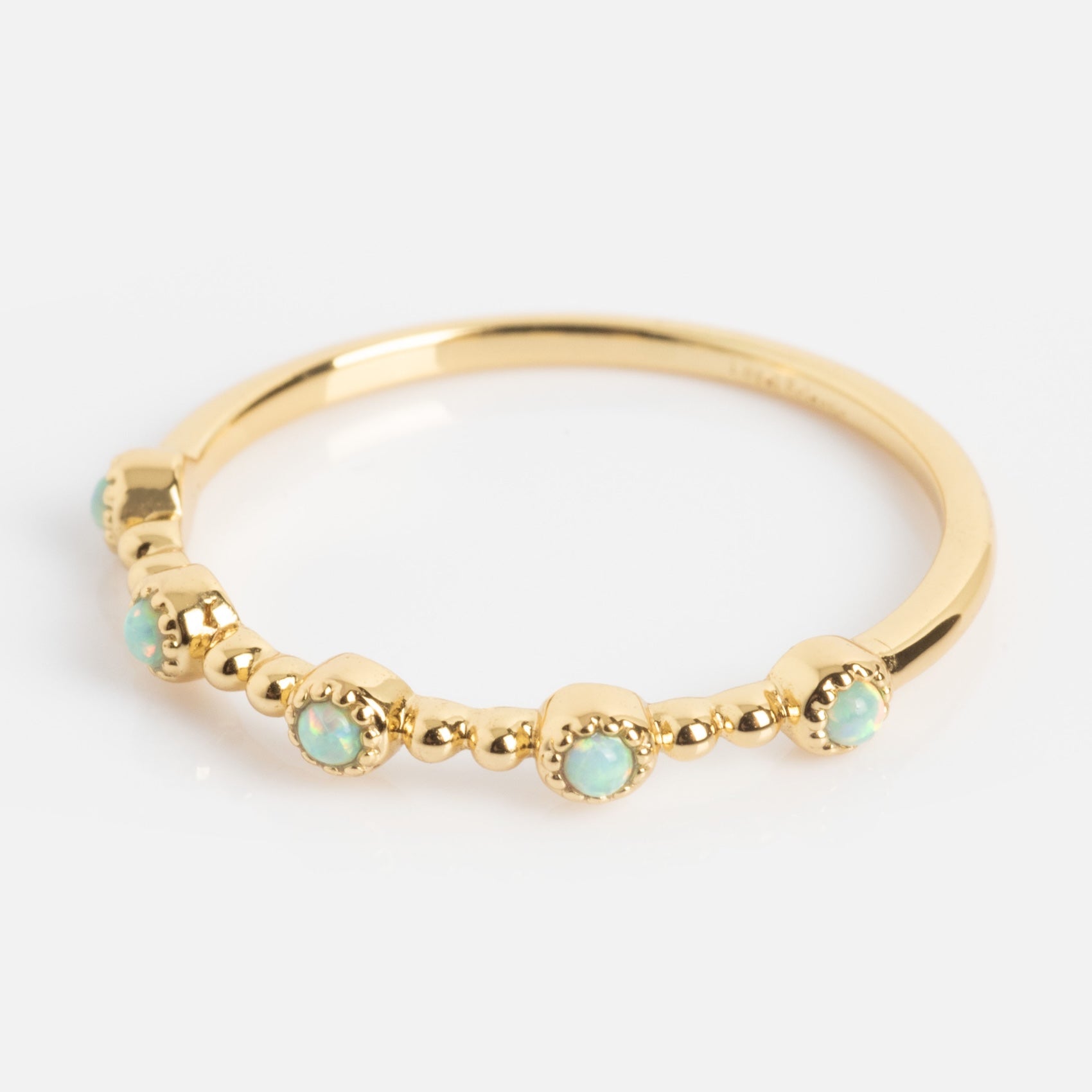 The Bezeled Beauty Stacking Ring is a delicate gold ring with small, round opal stones set in evenly spaced bezels along the band, shown on a plain white background.