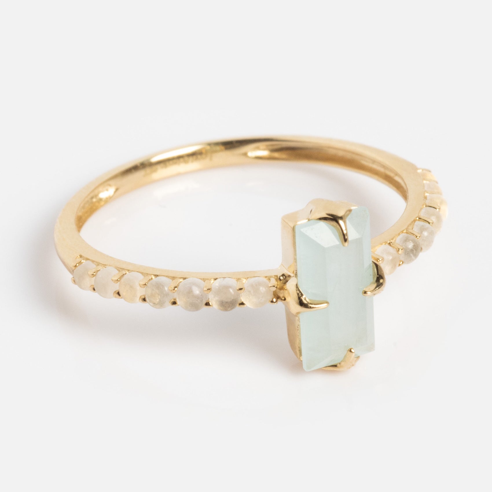 The 2026 March Capsule Delicate Aquamarine Solitaire Ring features a rectangular light green aquamarine at the center, accented by small round clear stones along the gold band, displayed on a white background.