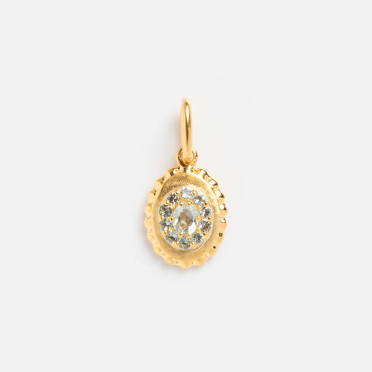 The 2026 March Capsule Vintage Inspired Aquamarine Charm is a small gold oval pendant with a textured edge, featuring a central aquamarine stone encircled by smaller clear stones and finished with a gold loop for attaching to a chain.