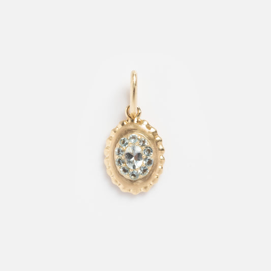 The Solid Gold 2026 March Capsule Vintage Inspired Aquamarine Charm is a small, oval gold pendant with a textured edge, showcasing a central aquamarine gemstone encircled by sparkling stones on a plain background.