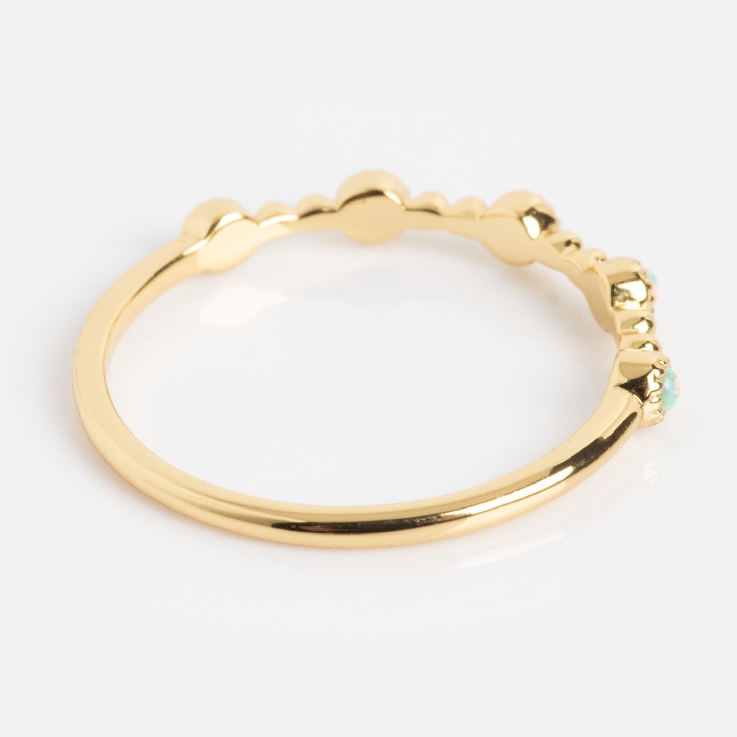 The Bezeled Beauty Stacking Ring features a smooth gold band with small rounded accents and a tiny gemstone set at one end, shown on a white background.