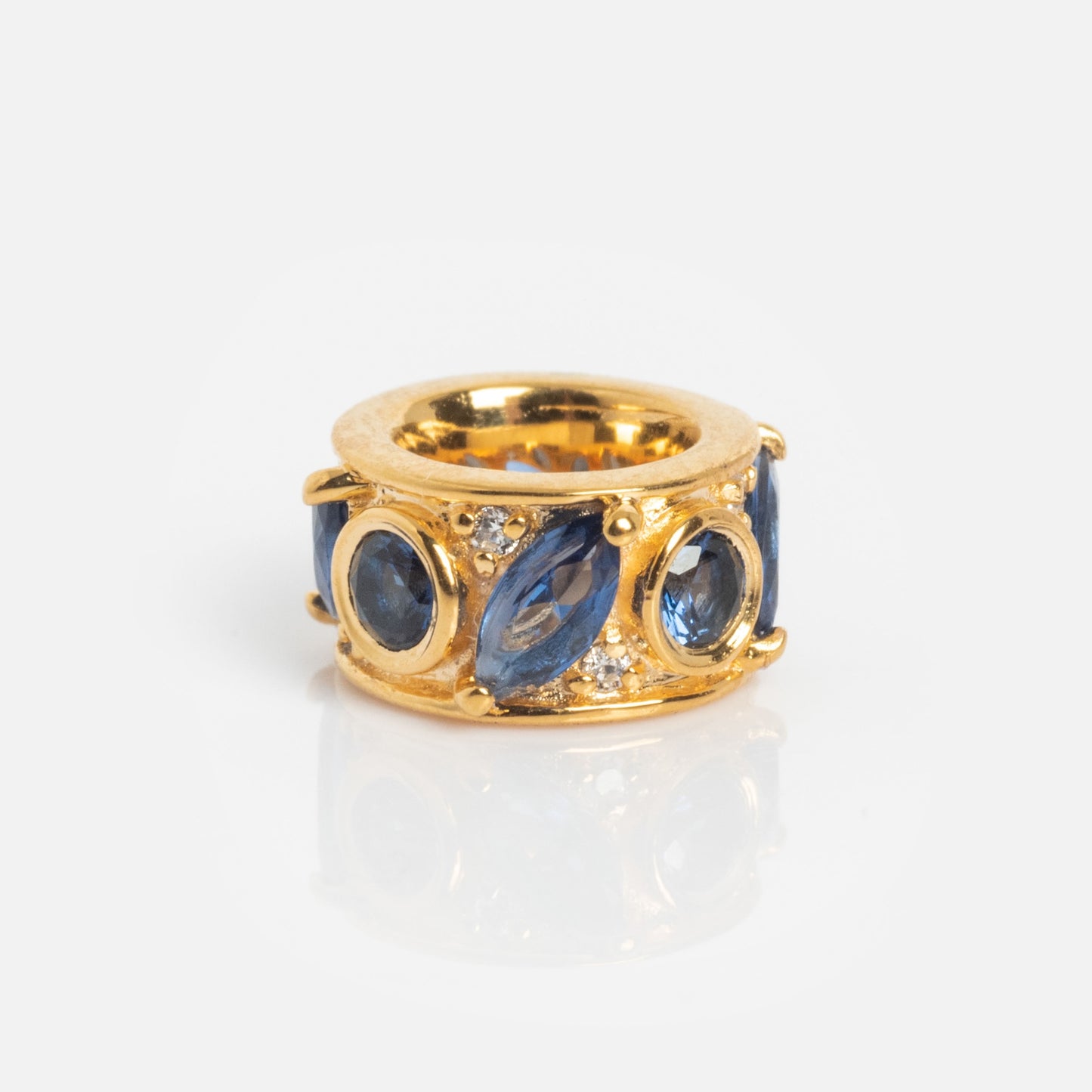 The Shades of You Birthstone Spacer Charm features oval and marquise-shaped blue gemstones with small round clear stones in an intricate setting, set on a wide band and shown on a white background.