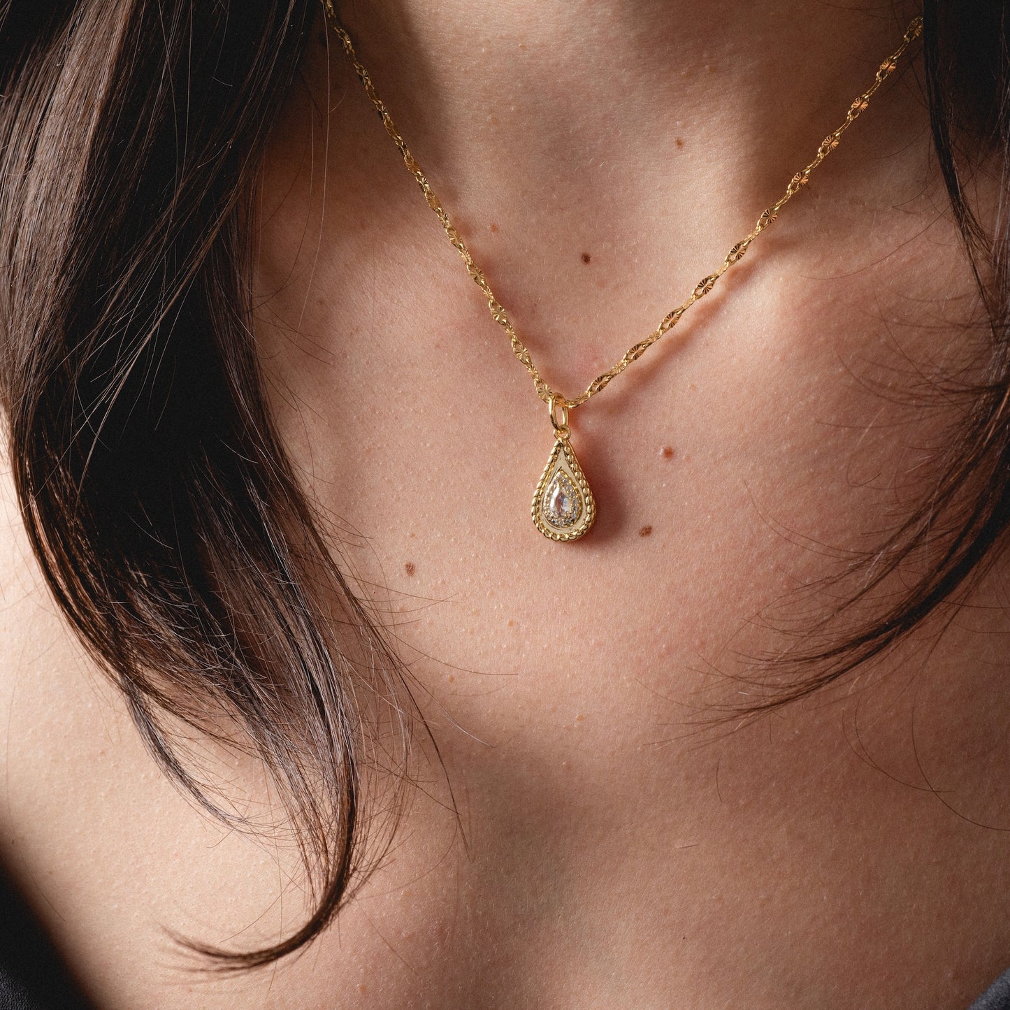 A close-up of a woman wearing the 2026 April Capsule Tethered Teardrop White Topaz Charm, a yellow gold vermeil necklace with the sparkling April birthstone pendant resting against her skin.